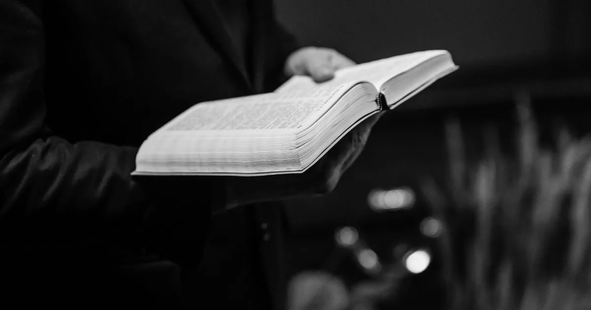 Person i dress som holder en oppslått bibel, i svart-hvitt