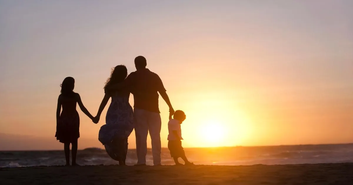 Silhuett av en familie som holder hender på en strand i solnedgang